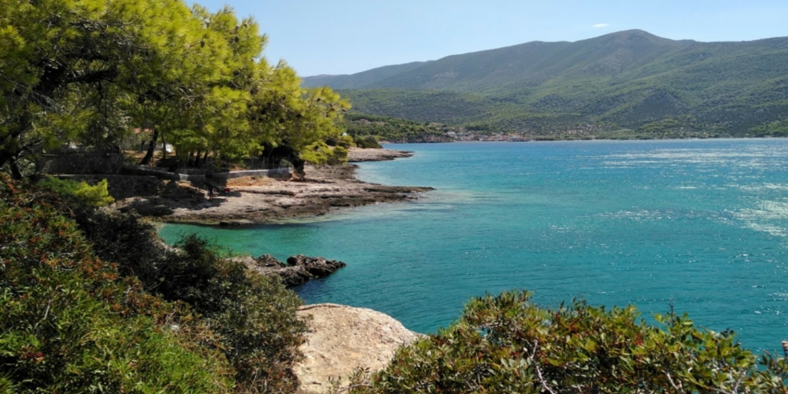 The beach with the blue waters and the tufted trees next to Athens
